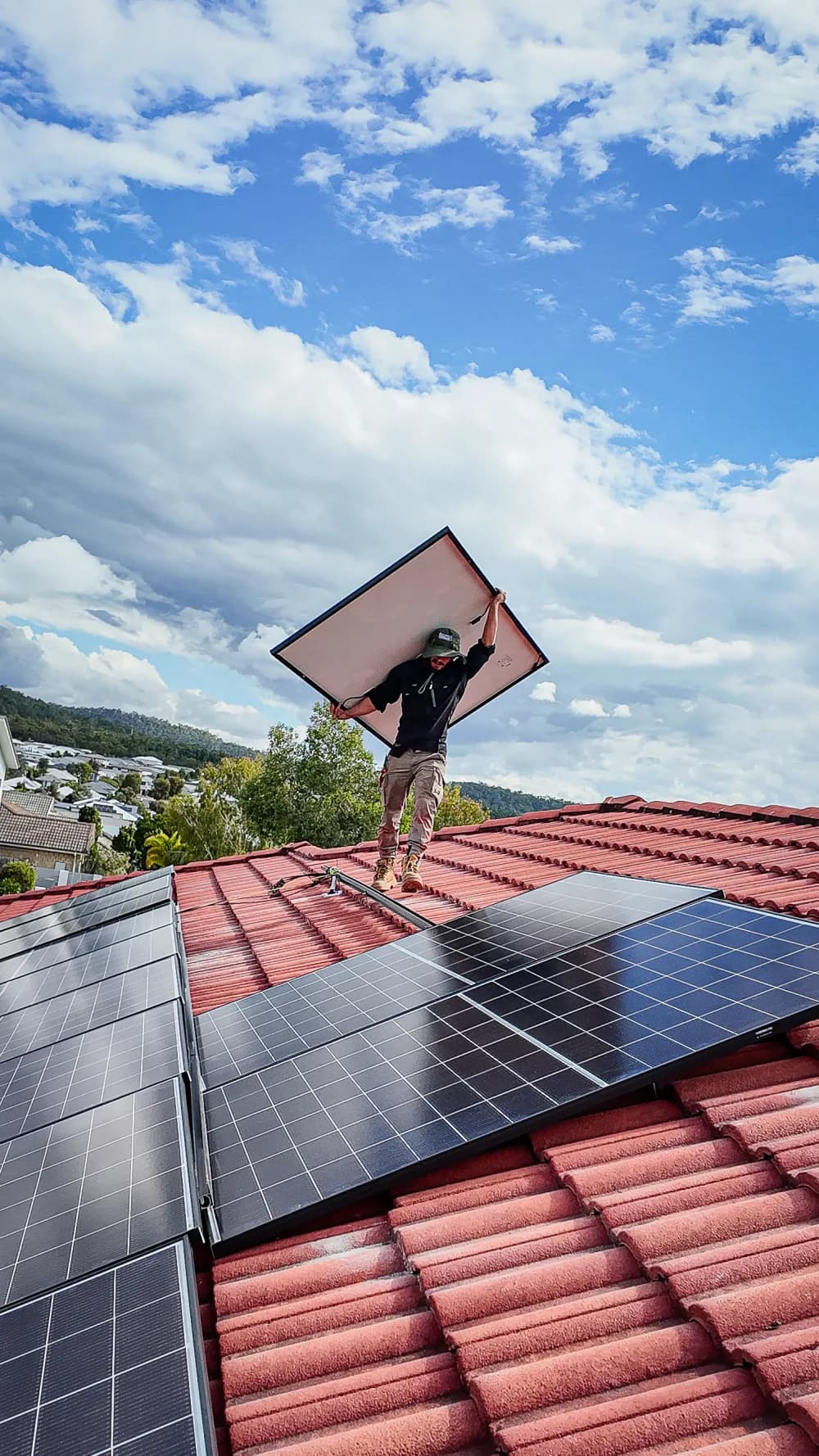 A Worth Solar Group installer carrying a panel over a finished rooftop array